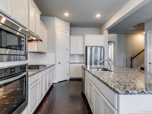 kitchen with dark wood-type flooring, stainless steel appliances, sink, tasteful backsplash, and an island with sink