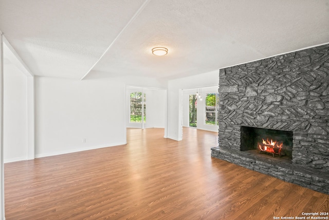 unfurnished living room featuring a textured ceiling, hardwood / wood-style flooring, and a stone fireplace