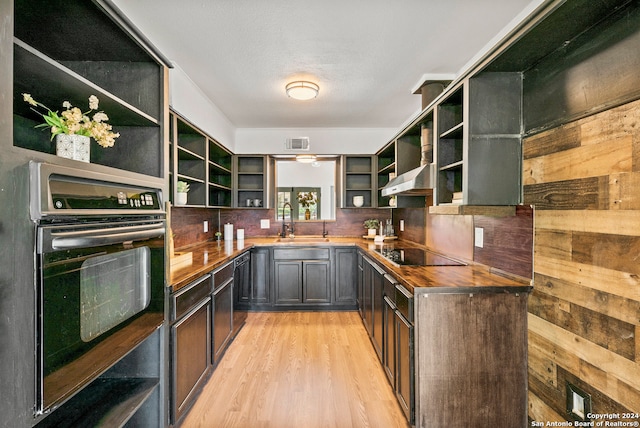 kitchen featuring butcher block countertops, light hardwood / wood-style floors, oven, wall chimney exhaust hood, and black electric stovetop