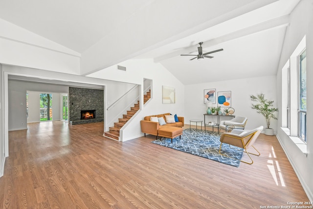 living room with beamed ceiling, hardwood / wood-style floors, ceiling fan, and a stone fireplace