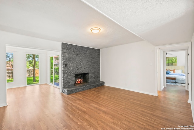 unfurnished living room featuring a wealth of natural light, a textured ceiling, hardwood / wood-style floors, and a stone fireplace