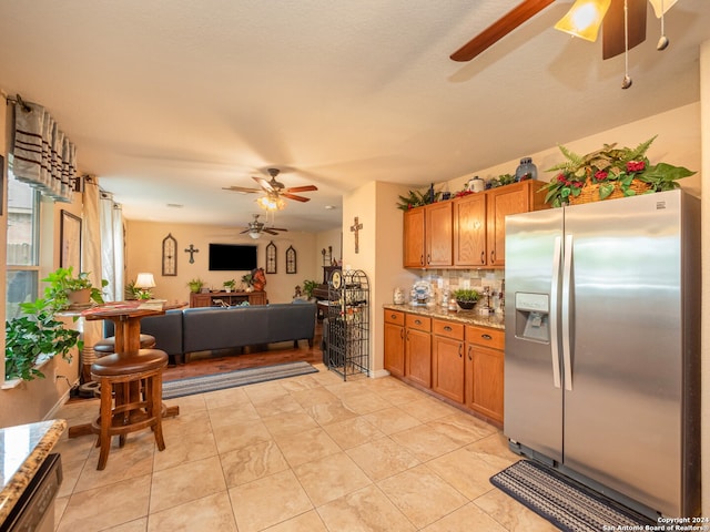 kitchen with stainless steel fridge, light tile patterned flooring, light stone countertops, and tasteful backsplash