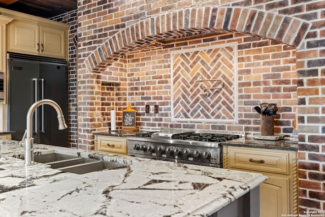 kitchen with cream cabinets, range, sink, brick wall, and stainless steel built in refrigerator