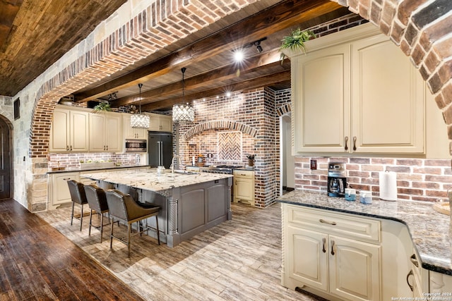 kitchen with a center island, built in appliances, hanging light fixtures, light stone countertops, and cream cabinets