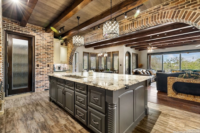 kitchen featuring beamed ceiling, ceiling fan with notable chandelier, sink, a center island with sink, and wood ceiling