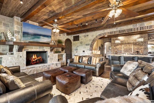 living room featuring wooden ceiling, ceiling fan, beamed ceiling, and a stone fireplace