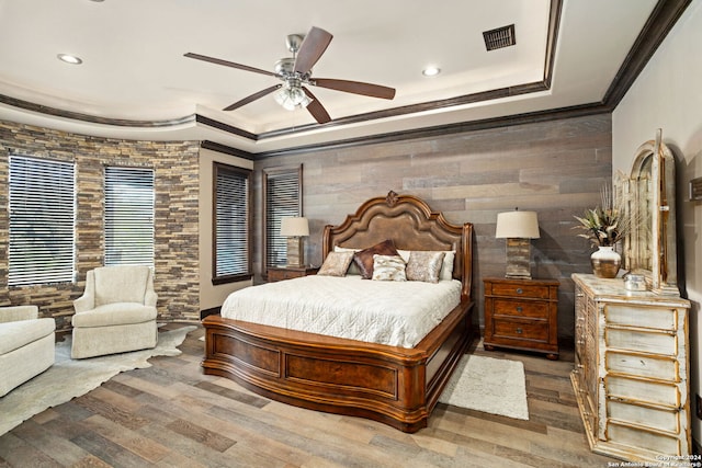 bedroom with ceiling fan, a raised ceiling, hardwood / wood-style floors, crown molding, and wooden walls