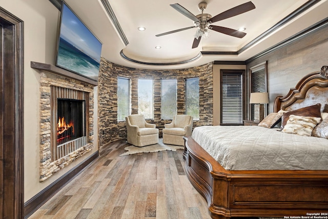 bedroom featuring a fireplace, a raised ceiling, ceiling fan, and hardwood / wood-style flooring