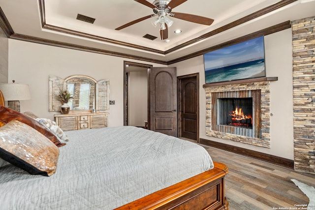 bedroom featuring ceiling fan, crown molding, hardwood / wood-style flooring, a fireplace, and a raised ceiling