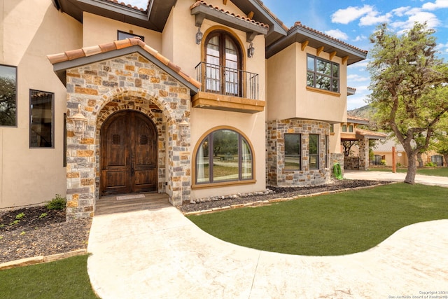 view of exterior entry with a balcony and a lawn