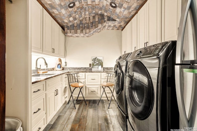 washroom featuring brick ceiling, cabinets, washer and dryer, wood-type flooring, and sink