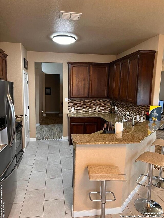 kitchen with stainless steel refrigerator with ice dispenser, tasteful backsplash, a breakfast bar, and light tile floors