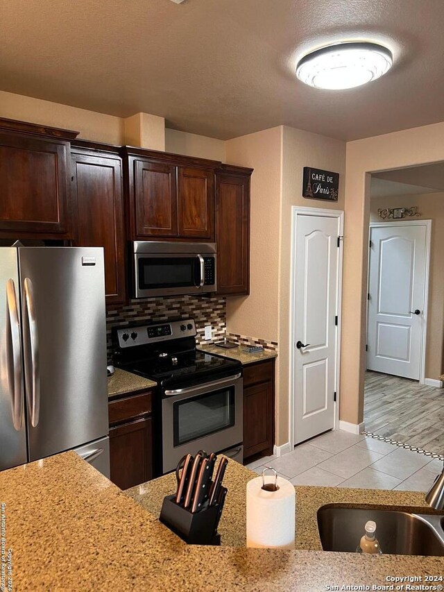 kitchen with light stone counters, appliances with stainless steel finishes, light tile floors, backsplash, and dark brown cabinets