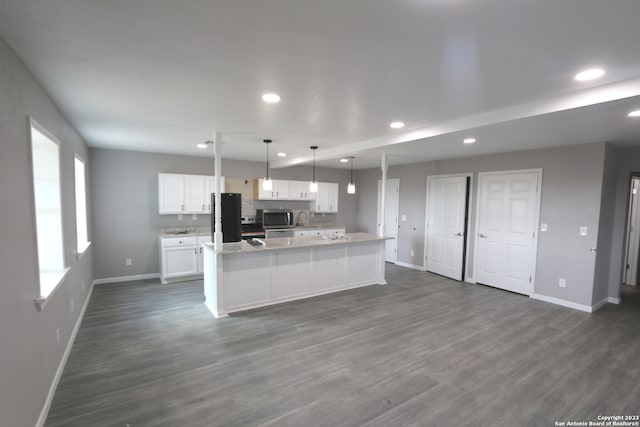 kitchen featuring dark wood-type flooring, white cabinetry, black fridge, hanging light fixtures, and a kitchen island with sink