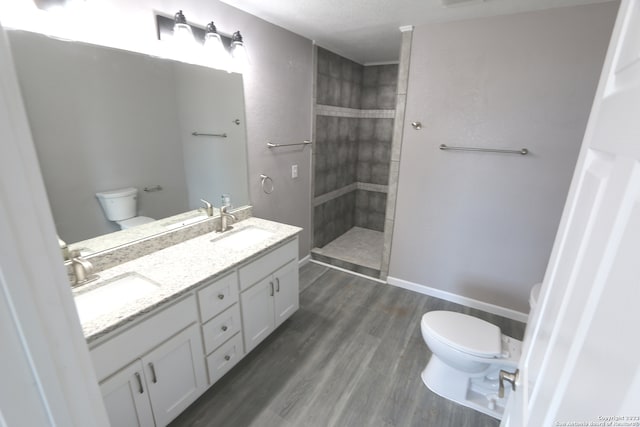 bathroom with tiled shower, wood-type flooring, toilet, and vanity