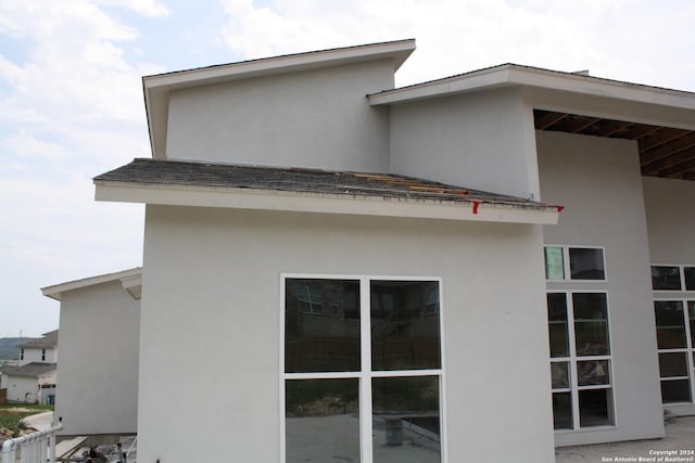 view of side of property with roof with shingles and stucco siding