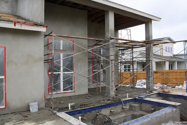 exterior space featuring an in ground hot tub, fence, and stucco siding