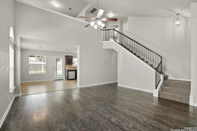 unfurnished living room featuring ceiling fan with notable chandelier, dark tile flooring, and high vaulted ceiling