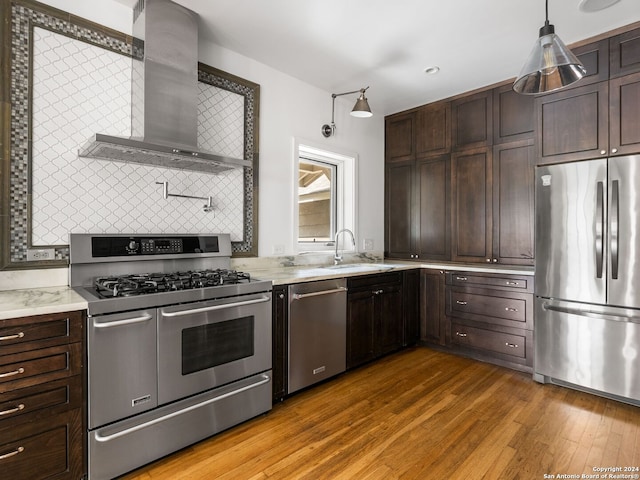 kitchen featuring wall chimney range hood, stainless steel appliances, decorative light fixtures, wood-type flooring, and sink