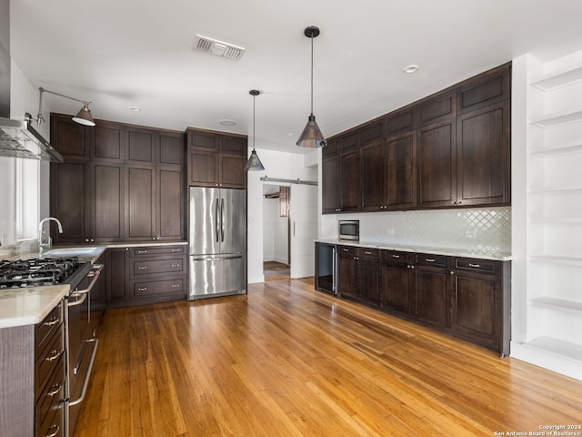 kitchen featuring tasteful backsplash, light wood-type flooring, pendant lighting, and appliances with stainless steel finishes