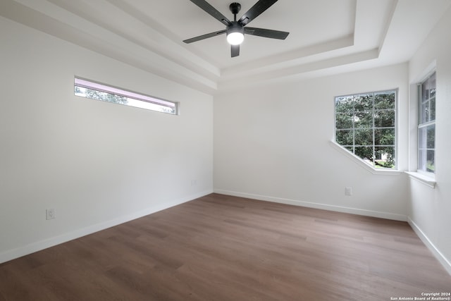 empty room with wood-type flooring, ceiling fan, and a raised ceiling