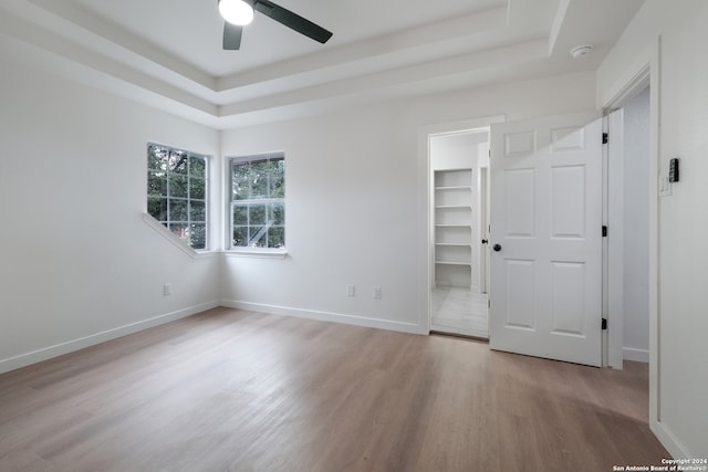 unfurnished bedroom with a closet, ceiling fan, a tray ceiling, hardwood / wood-style floors, and a spacious closet