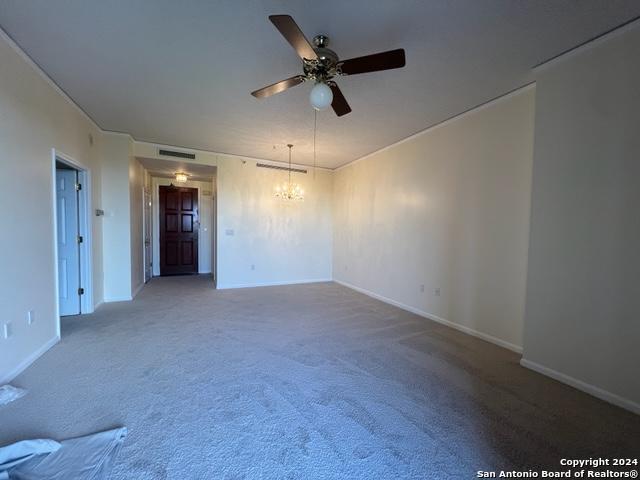 carpeted empty room featuring ceiling fan with notable chandelier