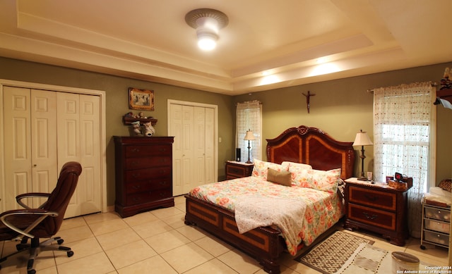 tiled bedroom featuring a raised ceiling and two closets