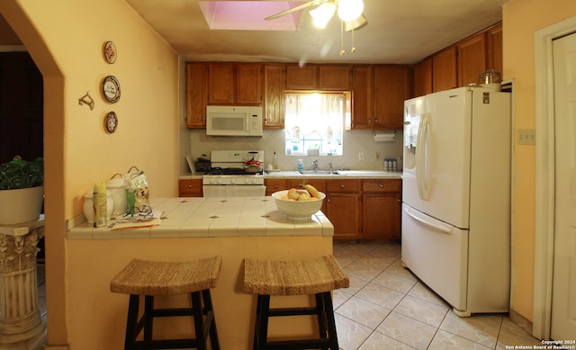 kitchen featuring tile counters, white appliances, backsplash, light tile floors, and ceiling fan