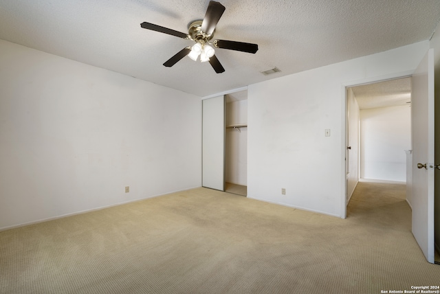 unfurnished bedroom featuring a textured ceiling, light colored carpet, ceiling fan, and a closet