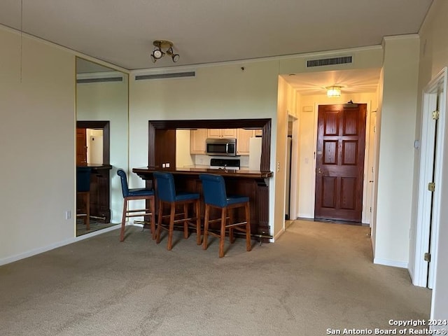 kitchen featuring ornamental molding, kitchen peninsula, light colored carpet, and a kitchen breakfast bar