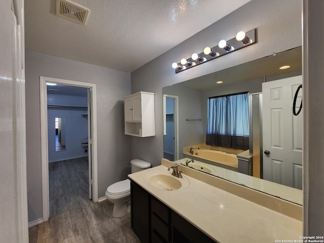 bathroom with a tub, wood-type flooring, a textured ceiling, toilet, and vanity