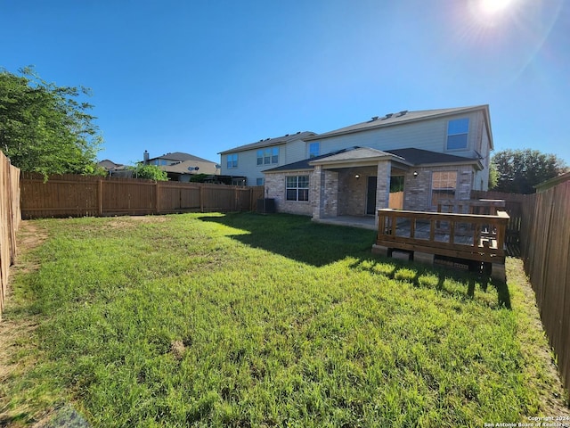 back of property with a deck, cooling unit, and a lawn