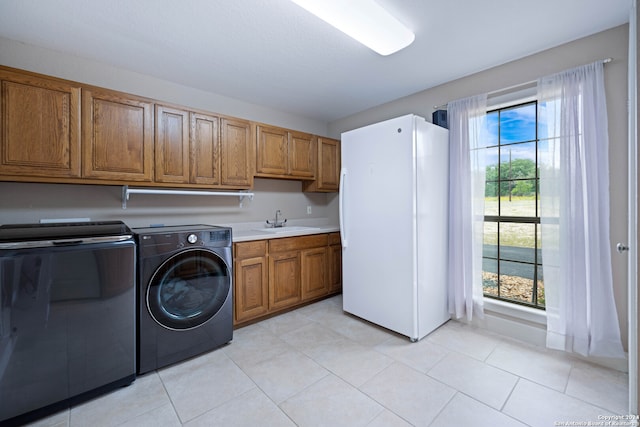 clothes washing area with cabinet space, light tile patterned floors, washing machine and dryer, and a sink