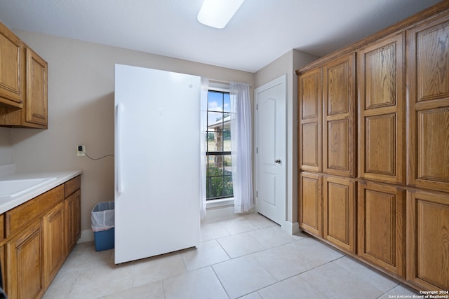 kitchen featuring light countertops, brown cabinetry, and freestanding refrigerator