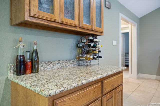 kitchen featuring light tile patterned flooring, brown cabinets, glass insert cabinets, and light stone counters