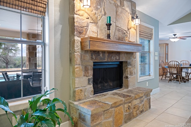 living room with ceiling fan, plenty of natural light, light tile patterned flooring, and a stone fireplace