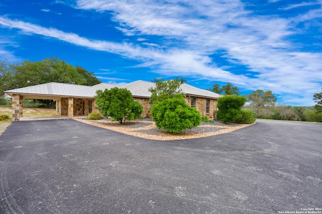 view of front of home featuring an attached carport, stone siding, driveway, and metal roof