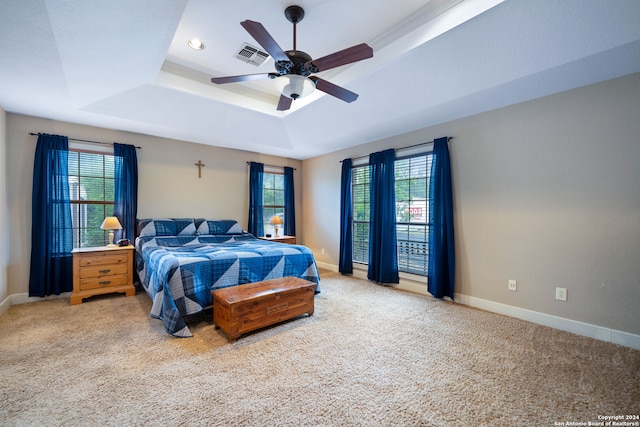 carpeted bedroom featuring a tray ceiling, ceiling fan, and multiple windows