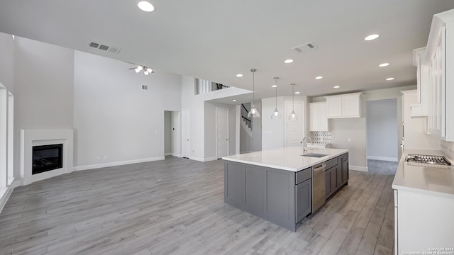 kitchen featuring light hardwood / wood-style floors, white cabinetry, stainless steel appliances, a center island with sink, and sink