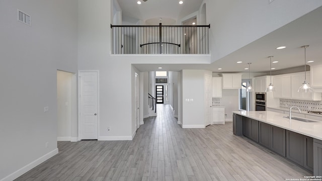 kitchen with sink, white cabinetry, light hardwood / wood-style flooring, a towering ceiling, and decorative light fixtures