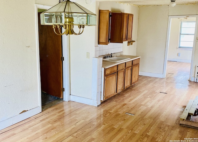 kitchen with tasteful backsplash, light hardwood / wood-style flooring, a notable chandelier, and sink