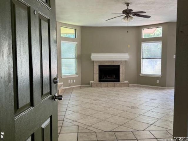 unfurnished living room featuring ceiling fan, light tile floors, and a tiled fireplace