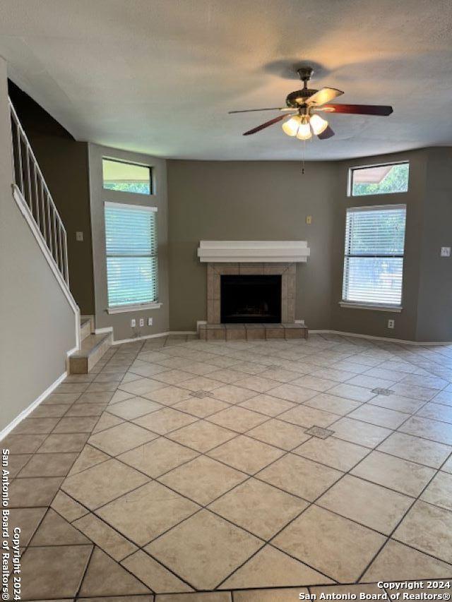 unfurnished living room featuring a fireplace, a wealth of natural light, ceiling fan, and light tile flooring