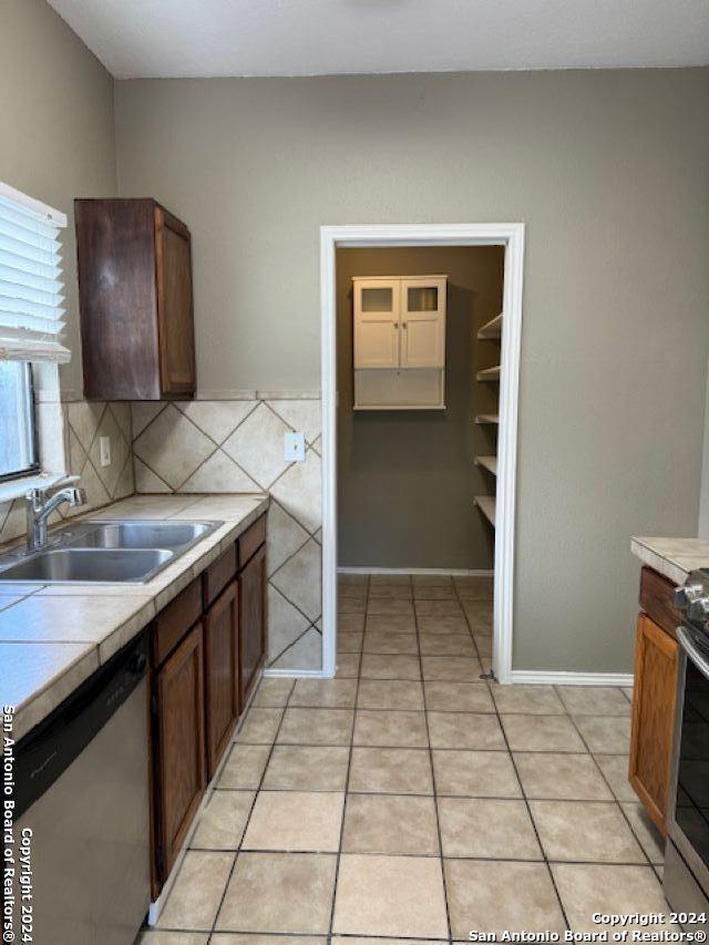 kitchen with light tile floors, sink, dishwasher, backsplash, and tile countertops