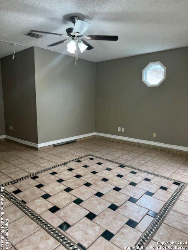 tiled empty room featuring ceiling fan and a textured ceiling