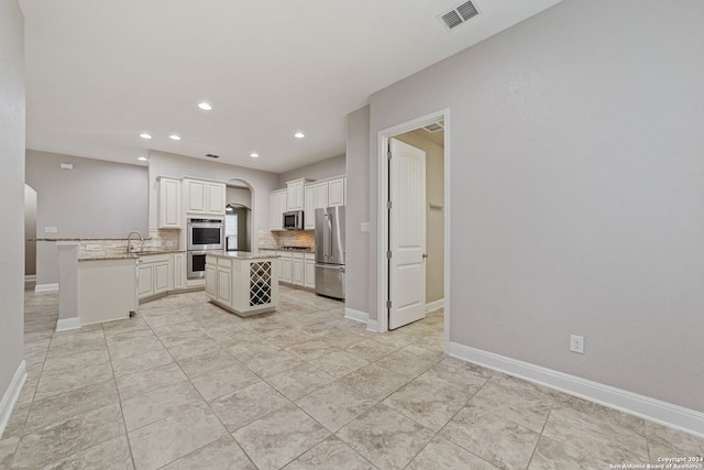 kitchen featuring backsplash, stainless steel appliances, white cabinetry, sink, and a center island