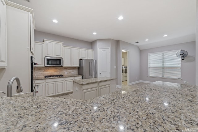 kitchen featuring light tile floors, washing machine and clothes dryer, white cabinets, stainless steel appliances, and light stone countertops