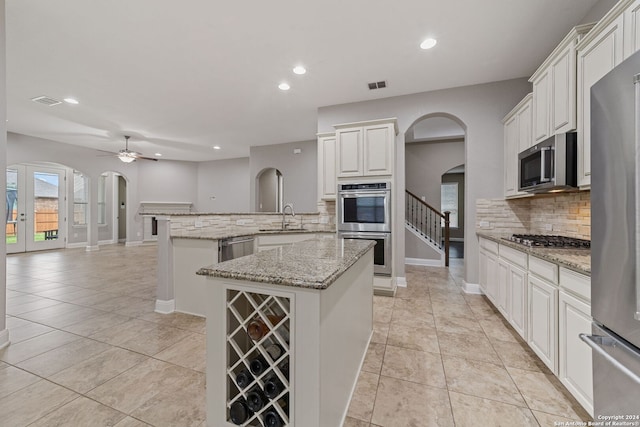 kitchen featuring light stone counters, appliances with stainless steel finishes, ceiling fan, backsplash, and white cabinetry