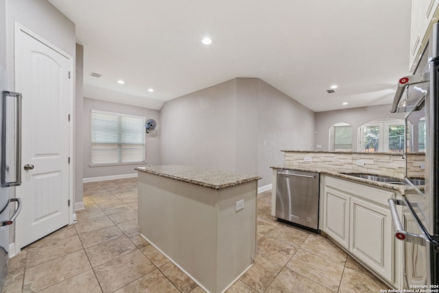 kitchen with a kitchen island, light tile floors, stainless steel dishwasher, and light stone countertops